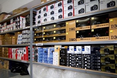 Warehouse shelving stacked with boxed cameras from Nikon, Canon and Fujifilm